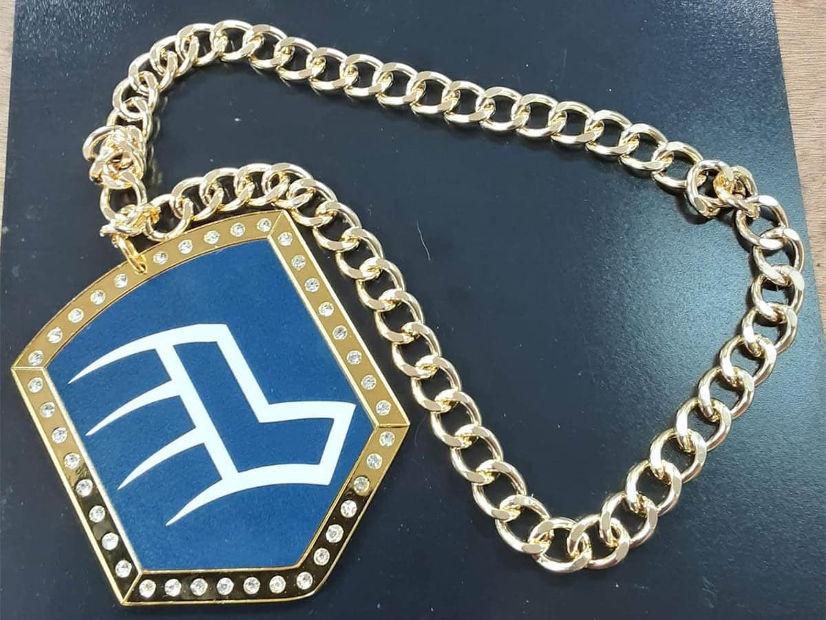 Custom championship shield chain with a stone-set blue shield medallion on a gold curb chain